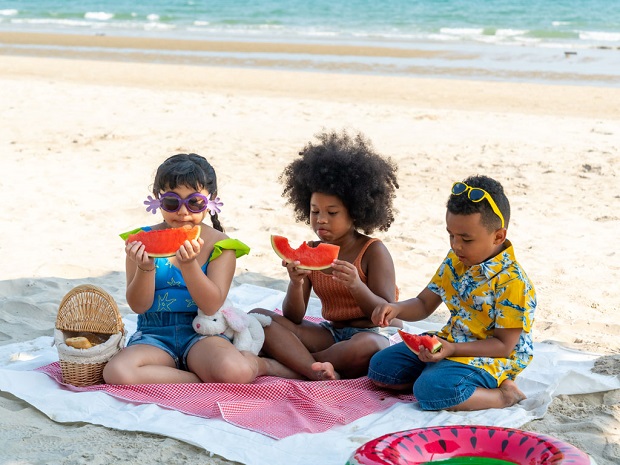 three little kids having picnic on the beach, eating watermelon