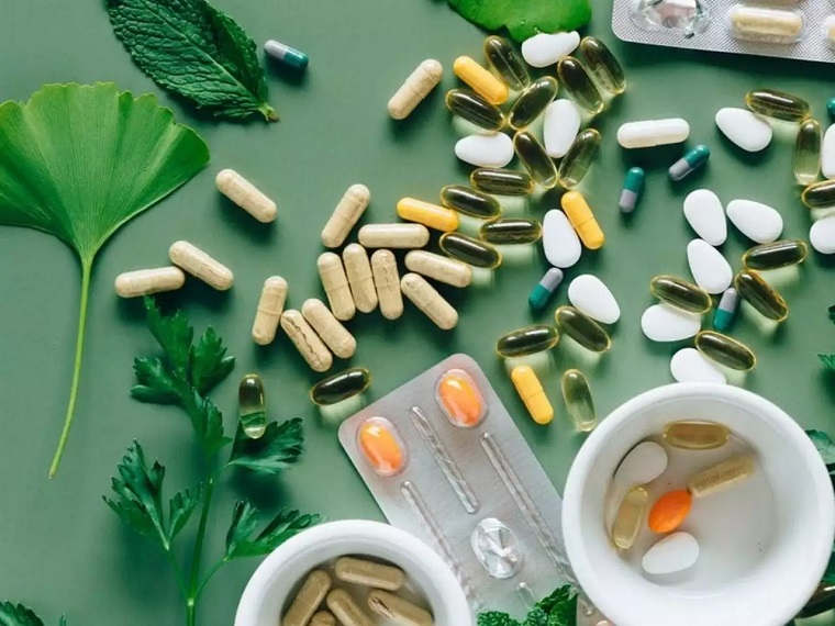 different types of vitamin capsules and pills surrounded by herbs and plant leaves