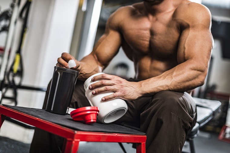 man scooping out creatine powder sitting on the bench at a gym